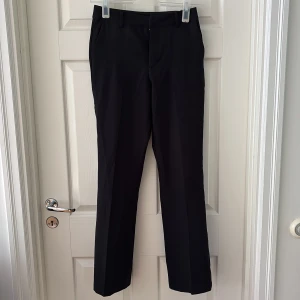 Svarta kostymbyxor - Snygga svarta kostymbyxor med bootcut-snitt och klassiska pressveck. Byxorna har hällor för bälte, sidfickor och två bakfickor. Perfekta för en clean och stilren look. Materialet känns mjukt och följsamt.