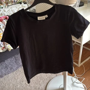 Svart basic t-shirt från Kappahl XS - En svart basic t-shirt från Kappahl i storlek XS. Klassisk rund halsringning och korta ärmar. Tillverkad i mjuk bomull, perfekt till jeans eller shorts. Enkel och stilren modell som funkar till allt.
