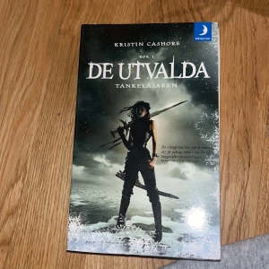 De utvalda: Tankeläsaren - Säljer boken 'De utvalda: Tankeläsaren' av Kristin Cashore. Det är en fantasybok på svenska med ett omslag som visar en mörkklädd karaktär med vapen i en snöig miljö. Perfekt för dig som gillar spännande äventyr och magi.