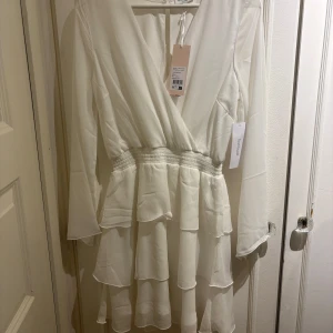 Studentklänning - Superfin studentklänning från bubbleroom! En vit omlottklänning med långa ärmar och v-ringning. Klänningen har volangdetaljer i kjolen och markerad midja med resår. Köpt till studenten 2024 men är helt oanvänd. Pris kan diskuteras (inköpspris 699)
