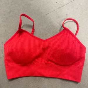 Röd ribbad linnetopp - Säljer en röd ribbad linnetopp med smala axelband. Toppen är stretchig och tillverkad i polyamid och elastan, vilket gör den bekväm och följsam. Perfekt att bära under en skjorta eller som den är.