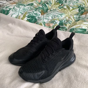 Svarta Nike Air Max 270 sneakers - Säljer ett par helsvarta Nike Air Max 270 sneakers med mesh-ovandel och synlig Air Max-dämpning i hälen. Skorna har snörning och en sportig design som passar perfekt till vardags och träning.