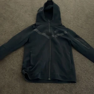 Nike tech svart hoodie storlek 150-160 - Hej jag har haft denna tröja på mig kanske 10 gånger och den är i perfekt skick. Den är i storlek 150-160 men passar även 165.