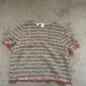 Färgglad topp - Säljer en kortärmad blus i tweed med rutigt mönster i grönt, orange och vitt. Toppen har fransiga kanter vid ärmslut och nederkant, super fina färger till sommaren!