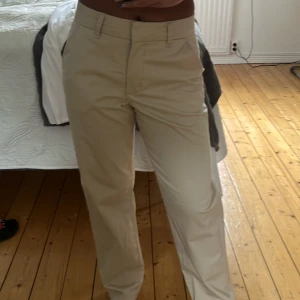 Beiga chinos med normal passform - Snygga beiga chinos med raka ben och klassisk design. Byxorna har hällor för bälte, diskreta fickor och stängs med dragkedja och knapp. Perfekta för en stilren look.