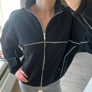 Cool cardigan 🖤 - Säljer en ascool svart cardigan med dragkedja och vita kontrastsömmar. Den är min syrras och är köpt på New Yorker för inte så länge sen🖤. Inga defekter, säljer då min syster inte använder den längre🥰. Passar mig som vanligtvis har storlek XS-M! (OBS ”fläcken” som syns på bilderna är pga att min spegel är smutsig…) 