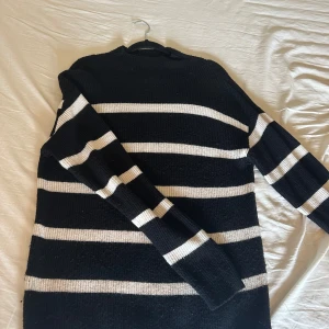 Svart och vit randig stickad tröja från Vila - Säljer en svart stickad tröja från Vila med vita horisontella ränder. Tröjan har lång ärm och mockneck-krage, perfekt för kyligare dagar. Mjuk och skön med klassisk look som passar till mycket. Är dock lite nopprig men det går ju snabbt bort med en nopprade.