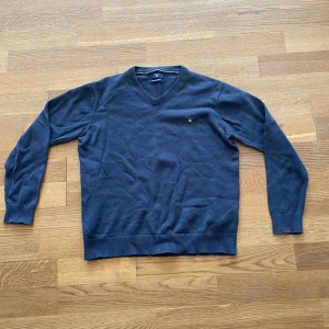 Mörkblå v-ringad tröja från GANT - Säljer en klassisk mörkblå v-ringad tröja från GANT i premium bomull. Tröjan har långa ärmar, ribbade muddar och en liten broderad logga på bröstet. Perfekt för en stilren och enkel look.