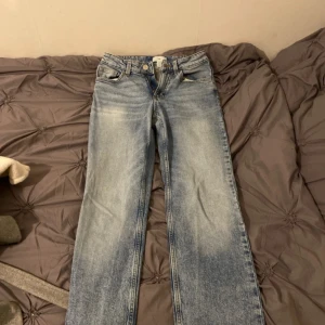 Blå raka jeans med ljus tvätt - Säljer ett par blå jeans med rak passform och ljus tvätt. Klassisk femficksmodell med normalhög midja och knappgylf. Perfekta till vardags för en avslappnad stil.