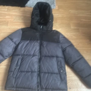 Svart och mörkgrå pufferjacka med huva - Säljer en svart och mörkgrå pufferjacka från Everest med huva och dragkedja. Jackan har lång ärm och två fickor framtill. Perfekt för kyliga dagar när du vill hålla dig varm och bekväm. Helt ny använt den 2 gånger.Jävligt snygg. 