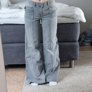 Ljusgråa wide jeans med låg midja - Säljer ett par ljusgråa jeans med vida ben och låg midja. Jeansen har klassiska fickor fram och bak samt en avslappnad passform. Perfekta för dig som gillar en loose och trendig stil. Sitter resår i i ryggen som går stt ta bort! Snabb affär prioriteras.