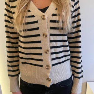 Beige och svart randig kofta med knappar - Säljer en beige kofta med svarta ränder och stora knappar framtill. Super fin men kommer tyvärr inte till användning.