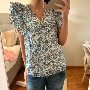 Blommig blus med puffärmar - Säljer en blommig blus i vitt och blått med v-ringning och voluminösa puffärmar. Blusen har ett romantiskt mönster och är perfekt för vår och sommar. Passformen är normal och materialet känns lätt och luftigt. 🩵 Orginalpris 890kr ca