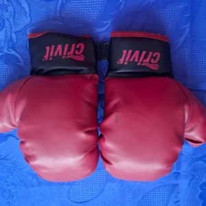 Röda och svarta boxningshandskar från Crivit - Säljer ett par boxningshandskar i rött och svart från Crivit. Handskarna har klassisk form med bred mudd och kardborreknäppning. Perfekta för träning och kampsport. Snygg design med röda detaljer och svart insida.