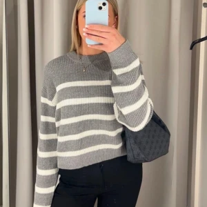 Gråvit randig stickad tröja från H&M - Säljer en stickad tröja från H&M i grått med vita ränder. Tröjan har en croppad passform, rund halsringning och långa ärmar. Har tyvärr inte kommit till användning och har ingen prislapp kvar, så den säljs nu. 🤍