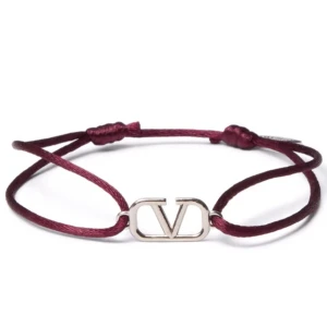 Vinrött armband med Valentino-logga - Säljer ett stilrent armband från Valentino Garavani med vinrött justerbart band och en silverfärgad logga i metall. Perfekt accessoar för att lyfta din outfit med en lyxig touch.