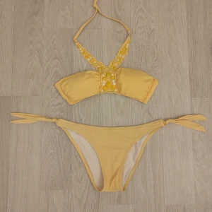 Gul bikini - Jättesöt gul bikini med broderade pärlor på överdelen och knyt i nacken samt knytning på sidorna av underdelen. Perfekt för stranddagar och sommarens bad. Väldigt bra skick.