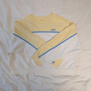 Gul och vit Levi's sweatshirt S - Sweatshirt från Levi's i storlek S. Tröjan är gul upptill och vit nedtill med blåa ränder och broderad Levi's-logga på bröstet. Långärmad och i mjuk bomull. Knappt använd så inga defekter🫶 skriv för frågor