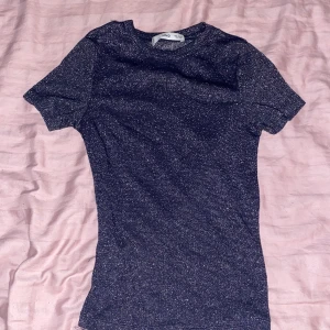 Glittrig mörkblå topp från MANGO  XS - Snygg mörkblå glittrig topp från MANGO i storlek XS. Modellen är slim och har korta ärmar samt rund hals. Materialet är mjukt och stretchigt. Använd 1 gång.