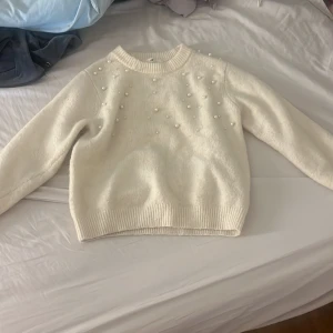 Vit stickad tröja med pärlor H&M - Superfin vit stickad tröja från H&M med pärldetaljer över axlar och bröst. Tröjan har rund halsringning, långa ärmar och ribbade muddar. Perfekt för att ge din outfit en söt och trendig touch. Köpt för 359 säljer för 20kr en liten slitning på ena armen inget som syns 