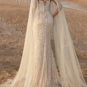 Champagnefärgad långklänning med pärlor - Magisk långklänning i champagnefärg med glittriga pärldetaljer och svepande tyllsläp från axlarna. Klänningen har en figurnära passform, markerad midja och breda axelband. Perfekt för bal eller nyår, med lyxig känsla och elegant design. Använd endast en gång i två timmar på en förlovning därför kommer den inte till användning nypris 2006kr 