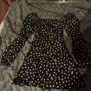 Svart blommig kortklänning från SHEIN - Supersöt svart kortklänning från SHEIN med vita blommor, puffiga långärmar och lätt markerad midja. Snörning vid bysten och dragkedja sitter på sidan 