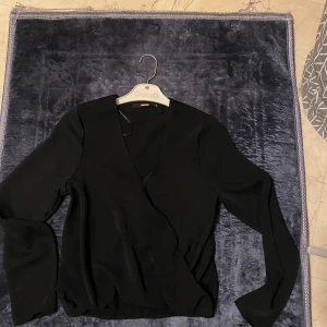 Svart omlottblus från BikBok - Säljer en svart omlottblus från BikBok i storlek S. Blusen har långa ärmar och en snygg v-ringning. Endast använd en gång. 