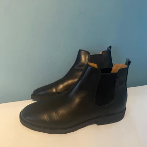 Svarta chelsea boots från Polo Ralph Lauren - Stilrena svarta chelsea boots från Polo Ralph Lauren i äkta skinn med elastiska paneler på sidorna och klassisk rund tå. Snygg kontrast med ljusbrunt innerfoder och robust svart sula. Perfekta för dig som vill ha en clean och tidlös look.
