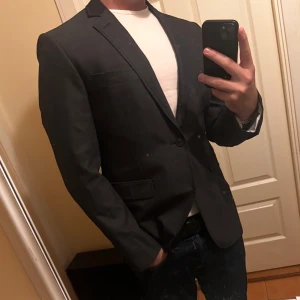 Mörkgrå kavaj från bläck - Snygg mörkgrå kavaj med enkelknäppning och smala slag. Kavajen har två fickor med lock och en bröstficka. Stilren design utan mönster, perfekt för dig som vill vara stiligast på klubben🍾