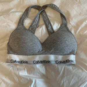 Grå sportig linnetopp Calvin Klein - Supersnygg grå linnetopp från Calvin Klein med brottarrygg och vit resår med logga. Perfekt för chill eller träning, mjukt material och stilren design. Sitter skönt och har en sportig vibe som funkar till många outfits. aldrig använd, 150kr