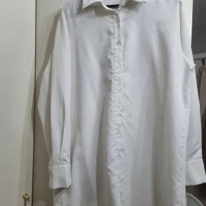 Vit klassisk skjorta med knappar - En stilren vit skjorta med lång ärm och klassisk krage. Skjortan har knäppning framtill och vid ärmslut, vilket ger en clean och tidlös look. Perfekt för dig som gillar enkel och snygg stil. Materialet känns mjukt och lätt mot huden.