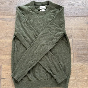 Mörkgrön stickad tröja These Glory Days - En stilren stickad tröja i merinoull från These Glory Days i en riktigt skön grön färg. Tröjan har rund halsringning, långa ärmar och ribbade muddar vid ärmslut och nederkant. Perfekt nu för hösten 🍁. Hör av dig vid minsta fundering 👍