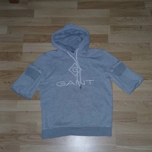 Grå hoodie från GANT med tryck - Snygg grå hoodie från GANT med vit logga framtill och klassisk huva med snörning. Tröjan har ribbade muddar och en känguruficka. Perfekt för en chill och avslappnad stil. Materialet är mjuk bomullsmix som känns skönt mot huden. Använd ett par gånger. 158-164cm. Köpt från GANT.
