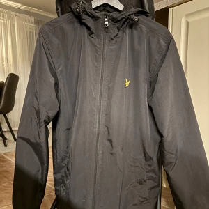 Svart vindjacka från Lyle & Scott M - Säljer en svart vindjacka från Lyle & Scott i storlek M. Jackan har huva med snörning, dragkedja framtill, helt oanvänd fick i present men hade redan köpt en ny jacka, pris kan diskuteras 