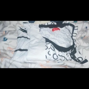 Randig gul och vit stickad tröja - Övre raden från vänster till höger: Grå svarta jeans (Lindex, modell Vicky strl 152/11–12y) Svarta tränings läggnings (söm har släppt där bak där lappen satt) Svart fuskpolo + orange/vit randig stickad långärmad crop top Ljuslila klänning med hål på sidorna + 2 maglinnen  Mellersta raden från vänster till höger: 3st pyjamaser med lång arm + ben  Raden längst ner från vänster till höger: 3st t-shirts som är välanvända som kan skickas med.  Allt är strl 146–152