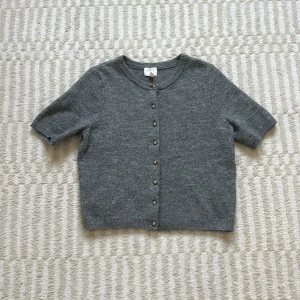 Grå kofta med korta ärmar och knappar - Kortärmad grå kofta från H&M med rund halsringning och snygga knappar framtill. Mjuk stickad känsla, perfekt till hösten🍂