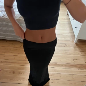 Svart långkjol i stretchigt material - Säljer en svart långkjol med figurnära passform och lätt utsvängd nederdel. Kjolen är enkel och stilren, perfekt att matcha med crop tops eller stickade tröjor. Materialet känns stretchigt och följsamt, vilket gör den bekväm att bära hela dagen.