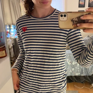Randig långärmad tröja Comme des Garçons - Säljer en klassisk långärmad tröja från Comme des Garçons Play med blå och vita ränder och det ikoniska röda hjärtat på bröstet. Tröjan är i  bomull och har en avslappnad passform. Tröjan är köpt här på Plick och flitigt använd av den tidigare ägaren. Jag har själv använt den 3-4 gånger. Jättefin!💙❤️🤍 Storlek M men skulle snarare säga S.
