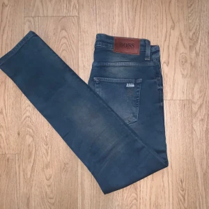 Blå slim fit jeans från Hugo Boss, storlek 31 - Snygga blå jeans från Hugo Boss i klassisk femficksmodell. Jeansen har en diskret tvättad look och raka ben. Märkespatch i läder baktill och metallmärke på bakfickan. Perfekta för dig som gillar stilrena och tidlösa jeans.