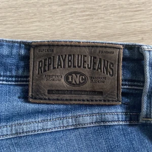 Replay Anbass blå jeans herr 33 - Säljer ett par Replay Anbass jeans i klassisk blå tvätt med slitna detaljer och snyggt broderad bakficka. Jeansen har normal passform och är tillverkade i mjukt bomullsjeansmaterial. Perfekta för dig som gillar en avslappnad men trendig look.