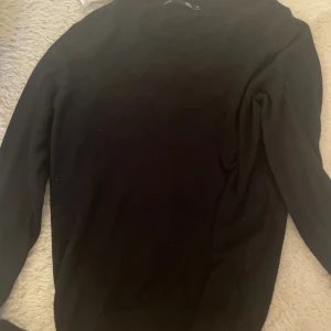 Svart stickad tröja från 157 - En svart stickad tröja från 157 i storlek S. Tröjan har rund halsringning med ribbade detaljer och långa ärmar. Enkel och stilren modell som passar perfekt till lager-på-lager under höst och vinter.