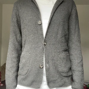 Grå Stickad Cardigan - Grå stickad cardigan perfekt för hösten! Modellen är 185cm 75kg och bär storlek M! Hör av er!