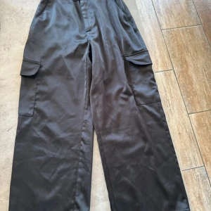 Svarta cargobyxor från Stradivarius - Svarta cargobyxor från Stradivarius med breda ben och stora fickor på sidorna. Byxorna har en loose fit och är tillverkade i ett mjukt, slätt material som känns skönt mot huden. Perfekta för en avslappnad och trendig look.