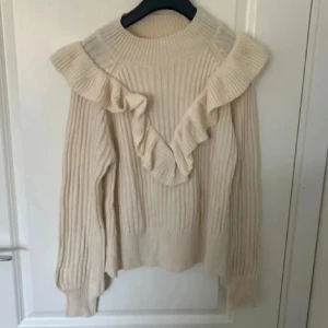 Beige stickad tröja med volang - Superfin beige stickad tröja med breda volanger över axlarna och framtill. 