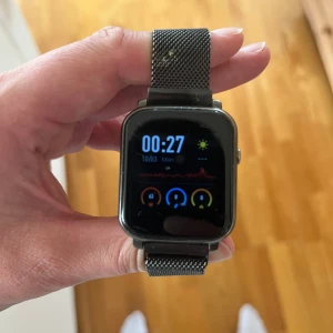 Svart smartklocka med mesh-armband - Snygg svart smartklocka med fyrkantig display och stilrent mesh-armband i metall. Klockan har touchskärm och funktioner som pulsmätare, sportläge, blodtryck, timer, musikstyrning och mer. Perfekt för dig som vill ha koll på både hälsa och notiser direkt på handleden. Medföljer ett extra armband och en laddare 