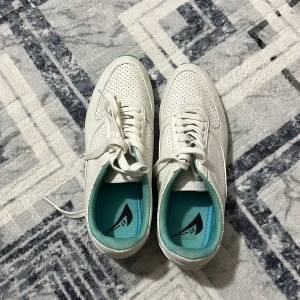 Vita sneakers med turkos innersula - Fräscha vita sneakers med perforerat mönster på ovandelen och turkosblå innersula. Skorna har klassisk snörning och rund tå, perfekt för en clean och sportig look. Passar dig som gillar stilrena och bekväma skor till vardags.