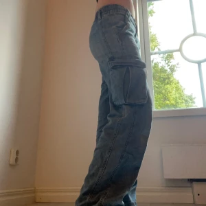 Blå cargopants från H&M Divided - Säljer ett par blå cargopants från H&M Divided i storlek 34. Byxorna har elastisk midja, stora sidofickor med lock. Perfekt för dig som gillar streetwear och vill ha mycket plats för prylar.