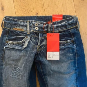Blå jeans från G-LAGG - Säljer ett par blå jeans från G-LAGG med coola slitningar och fransade detaljer vid fickor och midja. Jeansen har patchade partier på benen och dubbla knappar i midjan. Klassisk femficksmodell med snygg tvätt och raka ben. säljer då dom ör för korta för mig tyvärr (är 172 cm)