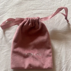 Rosa smyckespåse från Edblad - Söt rosa smyckespåse från Edblad med dragsko och satinband. Perfekt för att förvara dina favoritsmycken eller ge bort som present. Påsen har Edblad-loggan broderad i silver framtill och är mjuk och lyxig i känslan.
