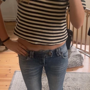 Blå jeans från BDG med låg midja - Säljer ett par klassiska blå jeans från BDG med låg midja och utsvängda ben. Jeansen har snygga slitningar och en metallogo på bakfickan. Tillverkade i jeansmaterial med en ljus tvätt som ger en avslappnad vibe.